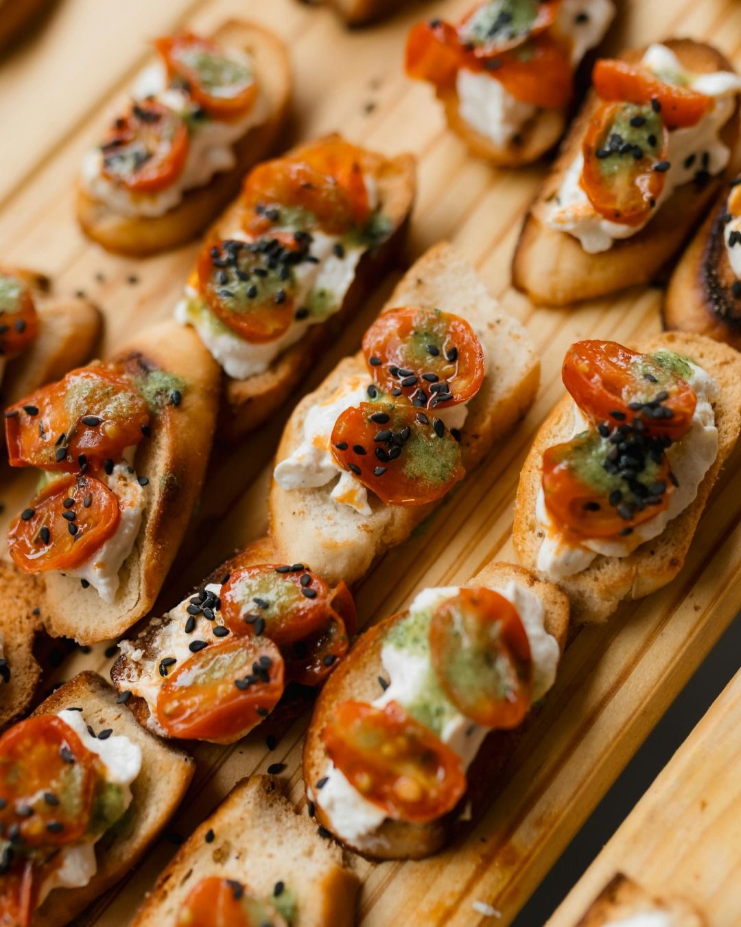 Toasted bruschetta topped with soft white cheese, roasted cherry tomatoes, herb oil and black sesame.