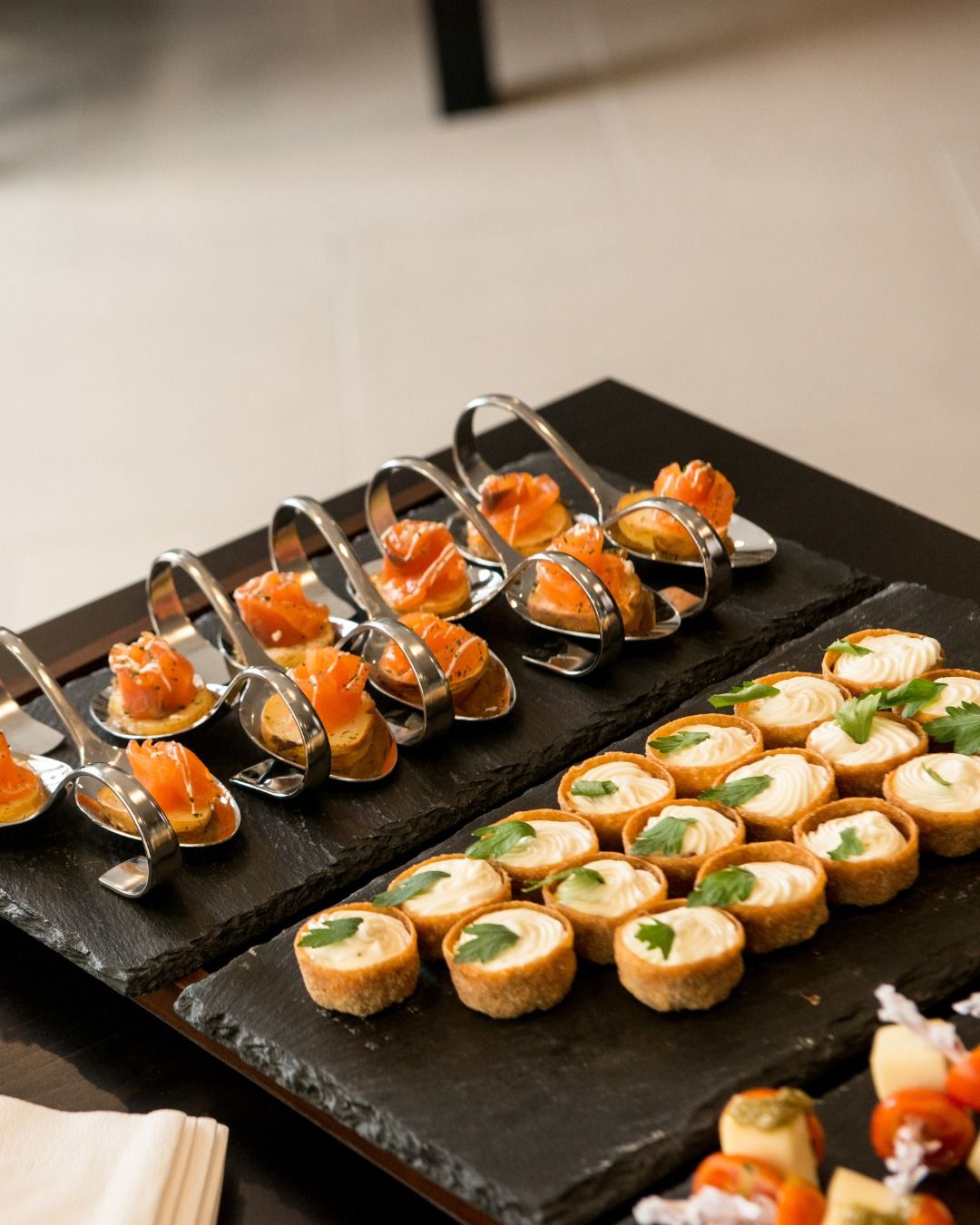 Canapés on slate: cured salmon on spoons and crisp pastry cups piped with a creamy filling.
