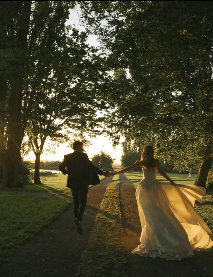 A couple run hand in hand down a tree-lined path at golden hour, her dress catching the low sun.